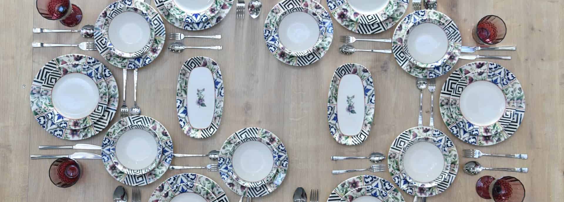 Çiçek desenli beyaz yemek takımı, siyah çizgiler ve bordo kadehlerle hazırlanmış bir sofranın üstten görünümü.