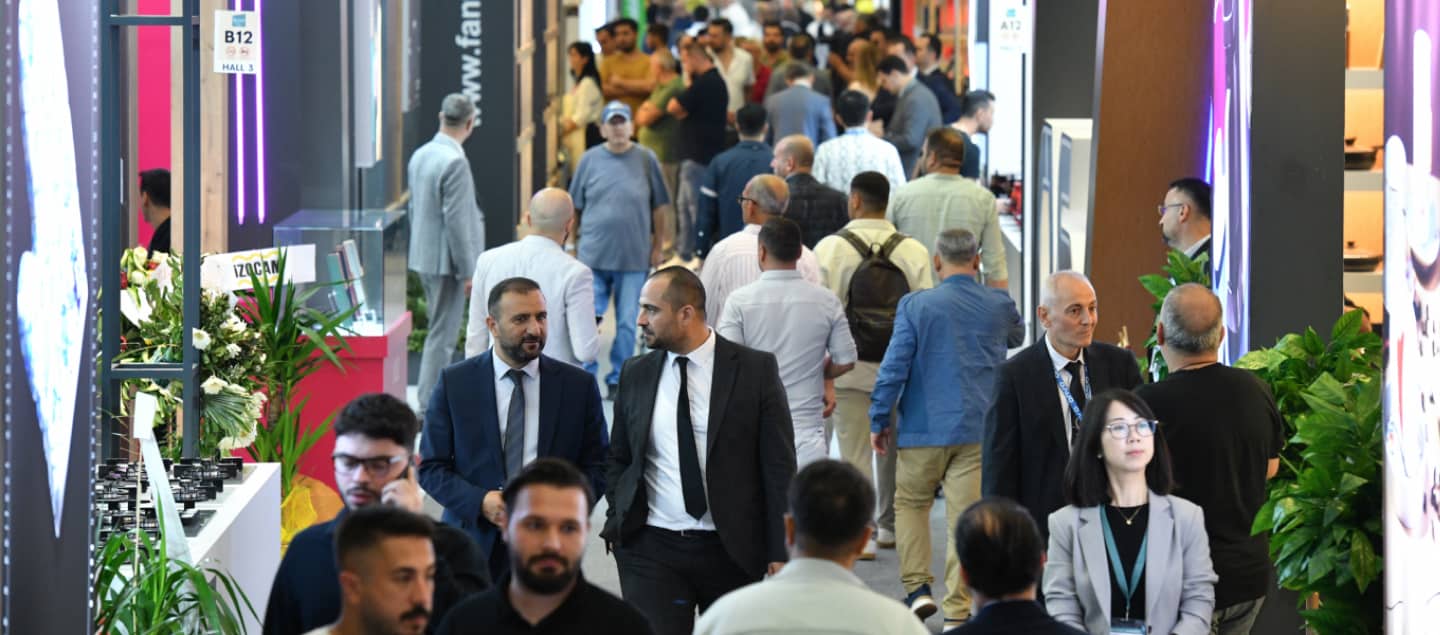 Fuarı ve marka stantlarını ilgiyle inceleyen ve salonda dolaşan kalabalık bir ziyaretçi grubu