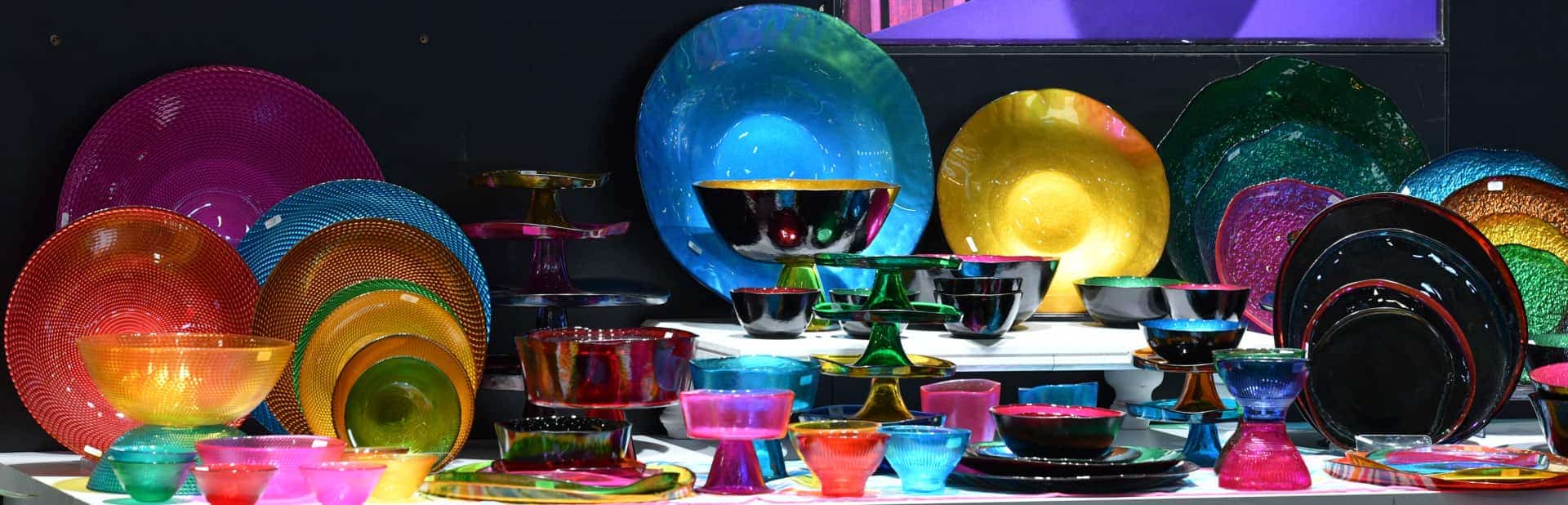 Canlı renklere sahip renkli cam sofra takımlarının sergilendiği ürün grubu.