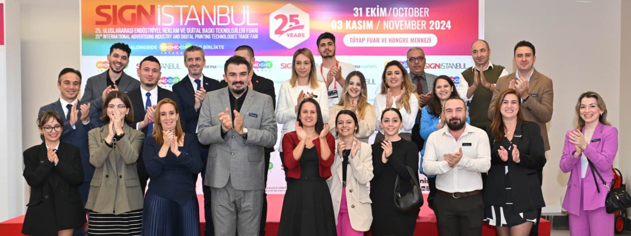 SIGN İstanbul team clapping in a group photo in front of the event signage, dressed in business attire