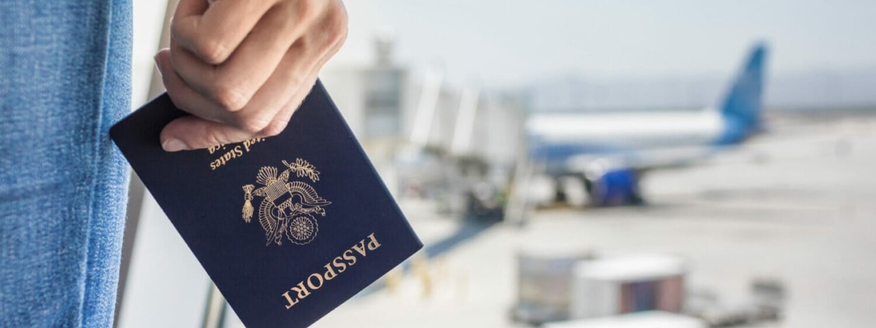 Closeup of a hand holding a passport at an airport with an airplane and luggage in the background