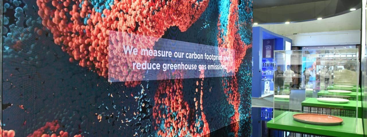 Katılımcı standının cam duvarında “Karbon ayak izimizi ölçüyor ve sera gazı emisyonlarını azaltıyoruz” yazıyor.