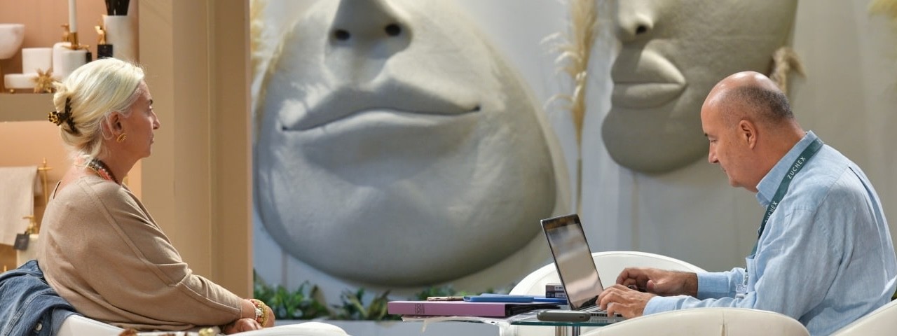 Yüz şeklinde tasarlanmış bir duvarın yanında, karşılıklı oturan iki ziyaretçi.