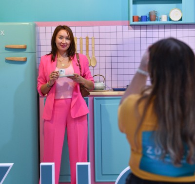  Bu yıl fuar için tasarladığımız renkli yapay ZUCHEX mutfağında, elinde bir fincanla poz veren mutlu bir ziyaretçi.