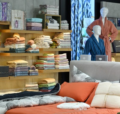 Turuncu-bej bir yatak, raflarda havlular ve rengarenk bornozlar giymiş heykeller.